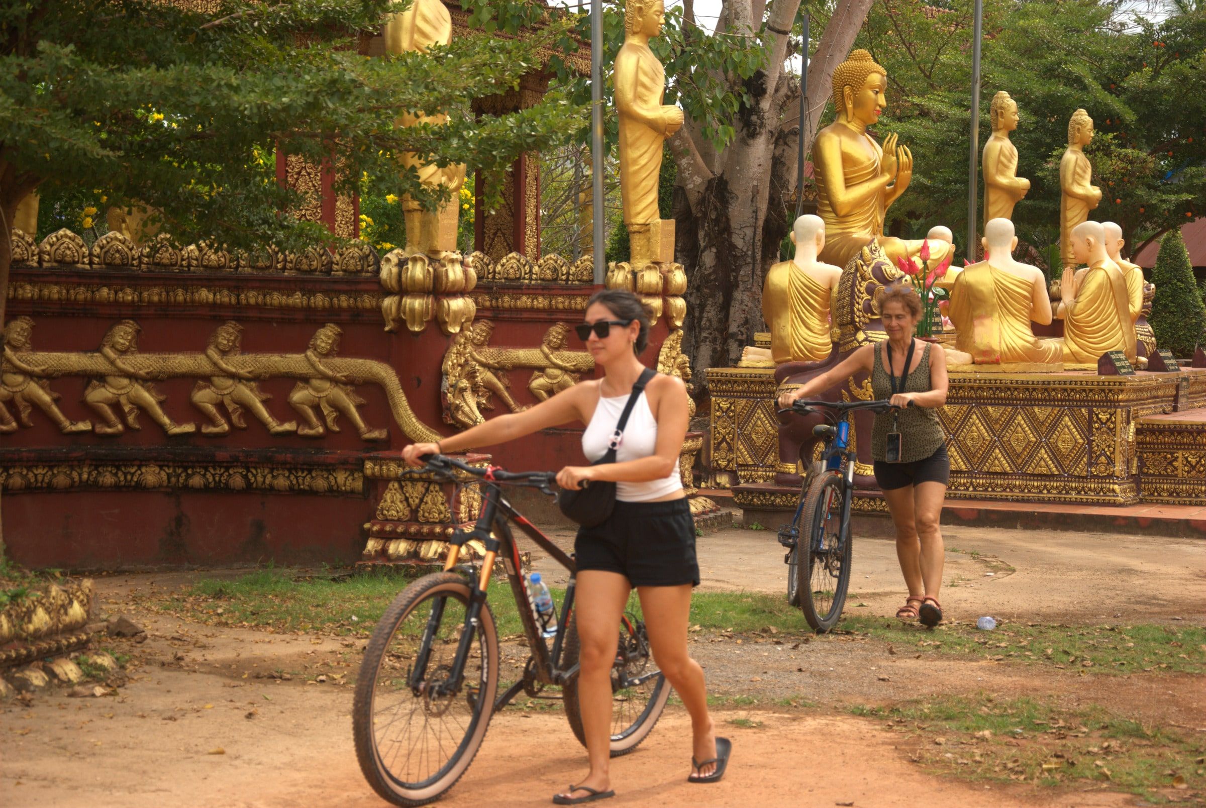 Two guests wheeling their bicycles past golden Buddha statues at a pagoda