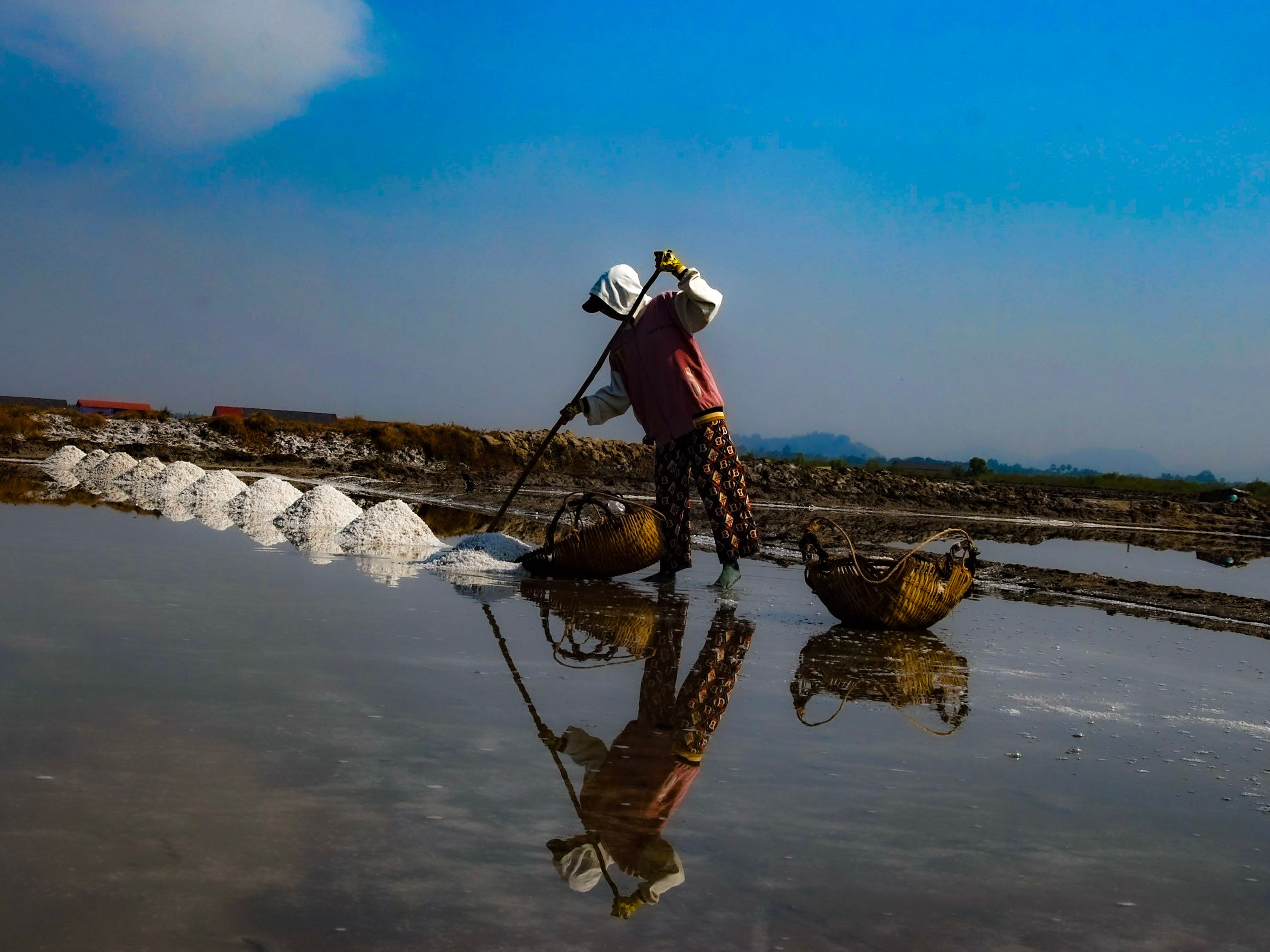 A worker raking salt into ridges, reflected in the flooded pan