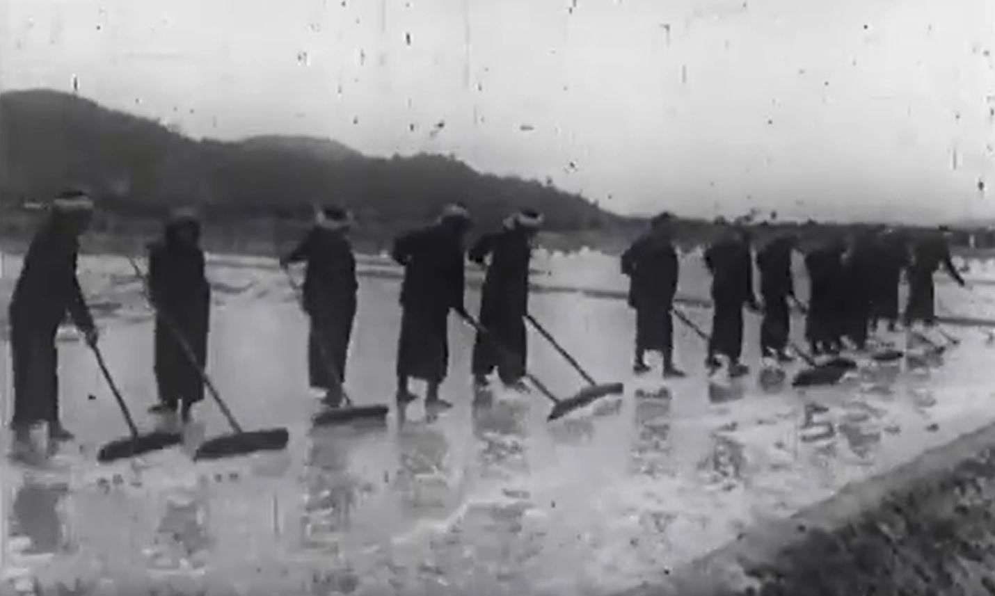 Archival black-and-white photo of a line of labourers raking Kampot's salt pans during the Khmer Rouge era
